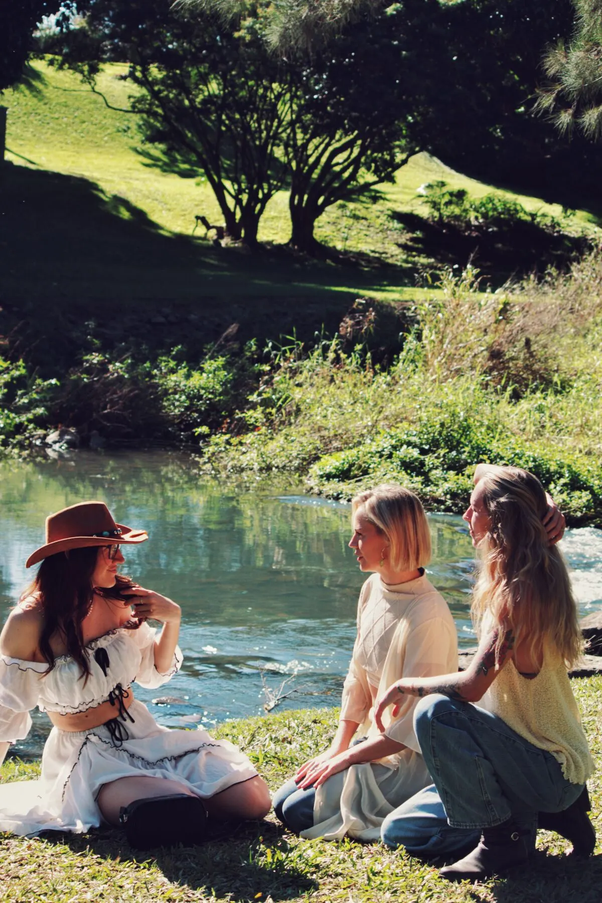 Three friends chatting on the grassy riverbank in the sun