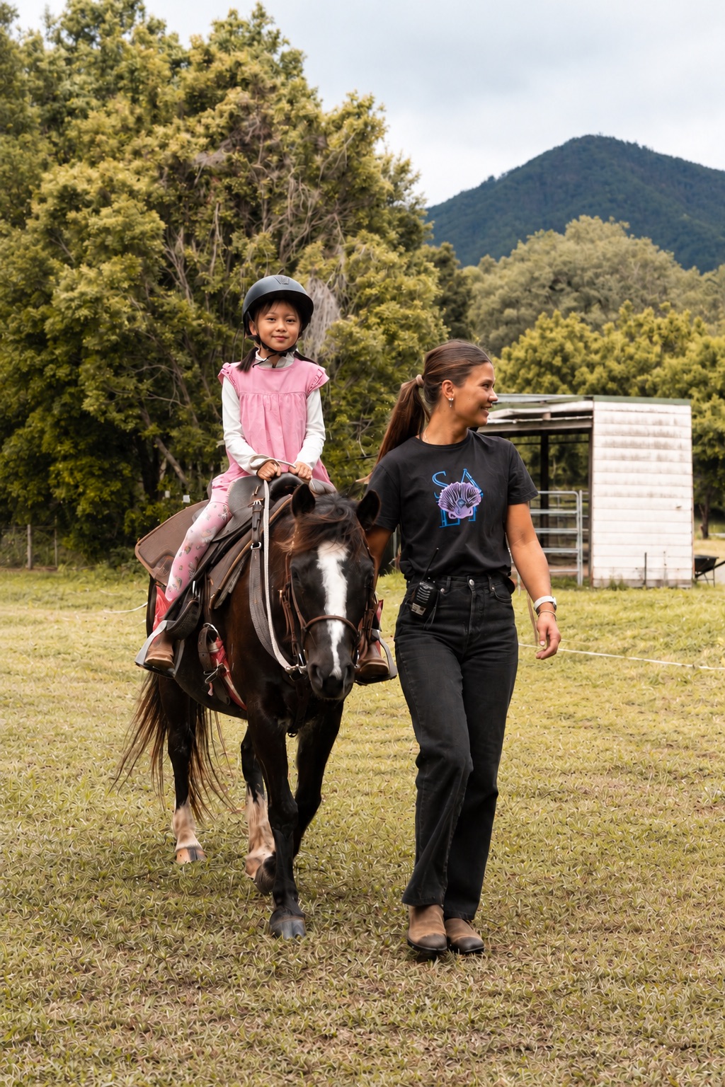 A young rider in a helmet aboard one of our gentle Paso horses, led by a handler