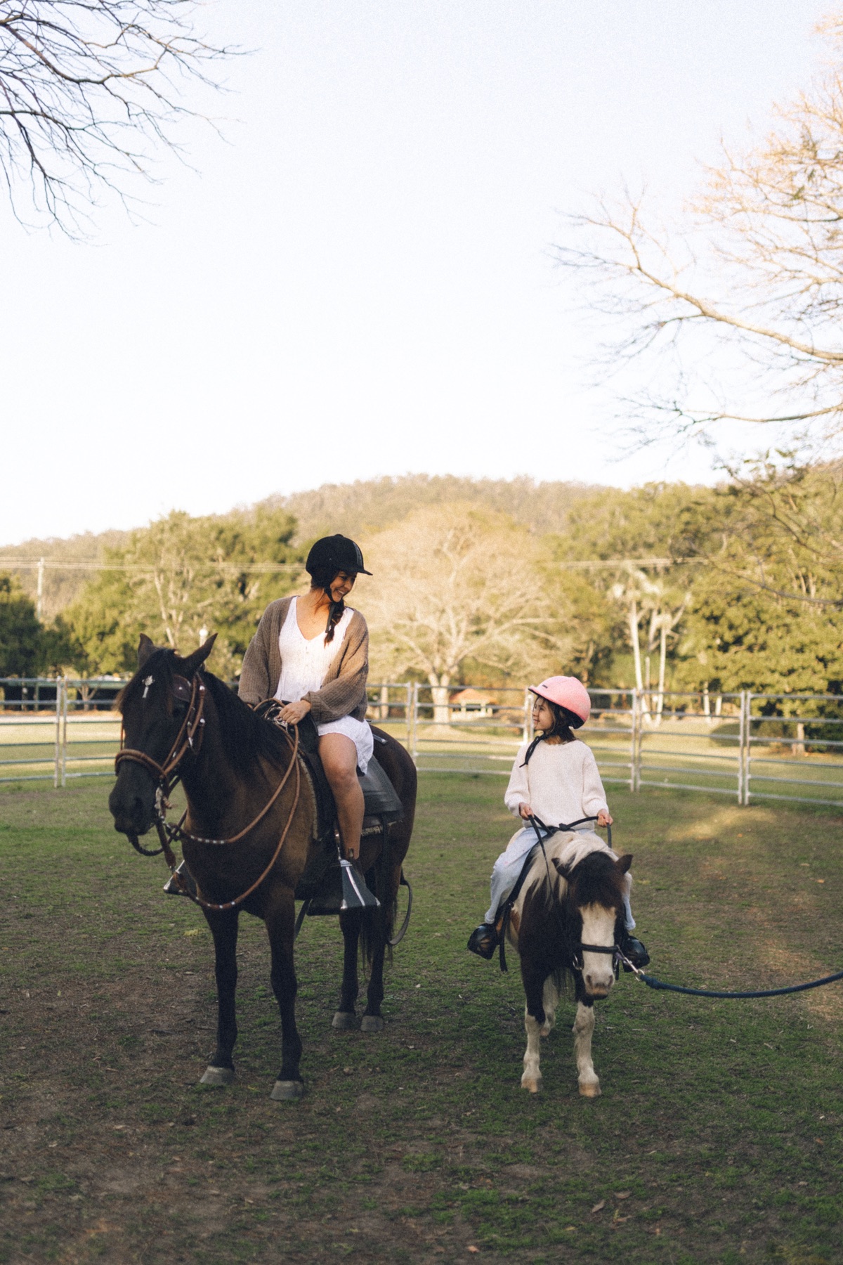 A woman on horseback and a child on a led pony in the paddock at Historic Rivermill